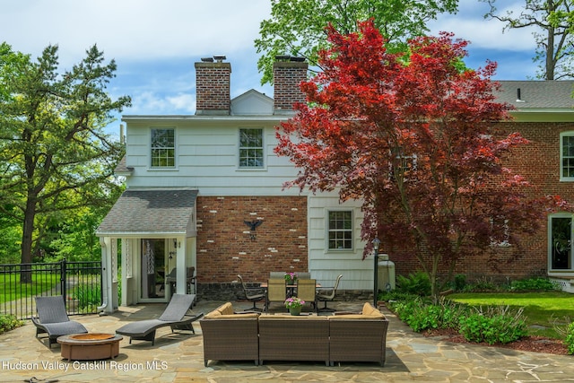 rear view of property featuring a patio area, a chimney, an outdoor living space with a fire pit, a shingled roof, and brick siding