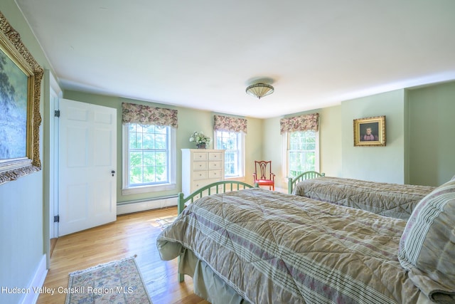 bedroom with baseboard heating, wood finished floors, and baseboards