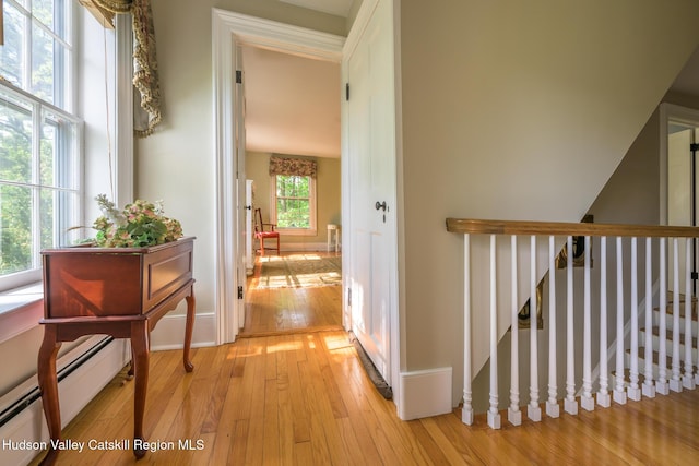 corridor featuring baseboard heating, light wood-type flooring, and baseboards