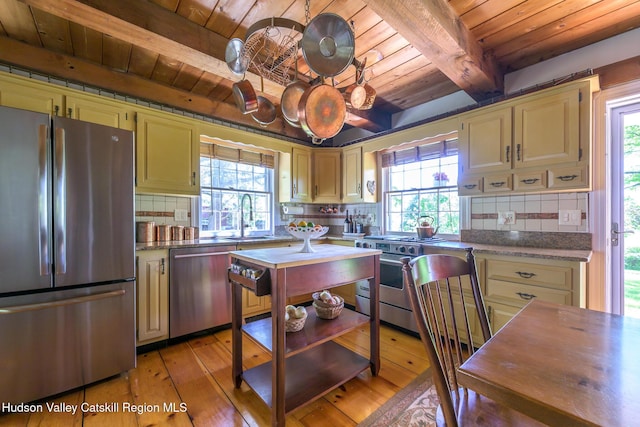 kitchen with appliances with stainless steel finishes, wood ceiling with exposed beams, a sink, healthy amount of natural light, and backsplash