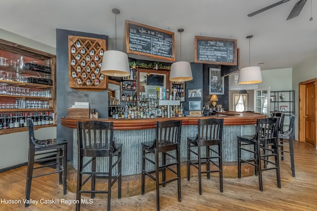 bar featuring a ceiling fan, wood finished floors, and a bar