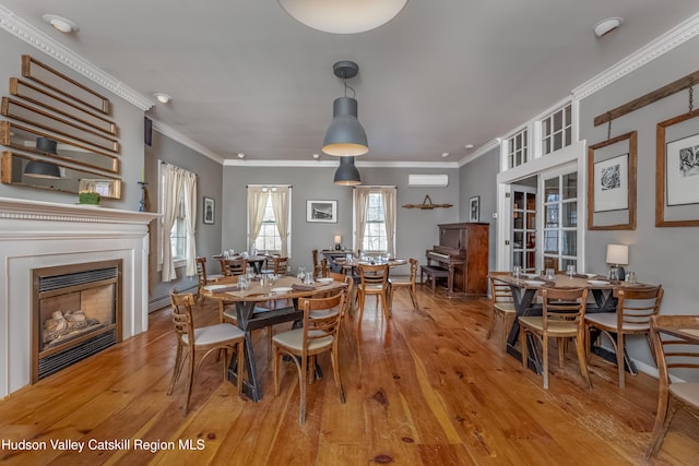 dining area with hardwood / wood-style floors, a glass covered fireplace, an AC wall unit, and crown molding