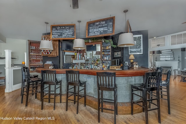 bar with a dry bar, wood finished floors, a fireplace, and decorative columns