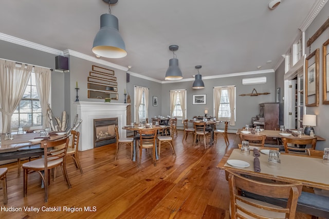 dining area with a glass covered fireplace, light wood-style flooring, a wall mounted AC, and crown molding