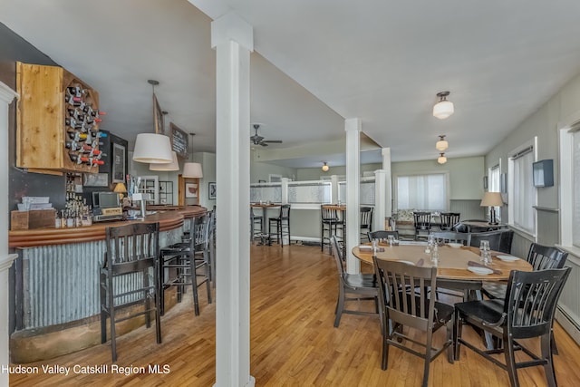 dining space with wood finished floors, a dry bar, ornate columns, and ceiling fan