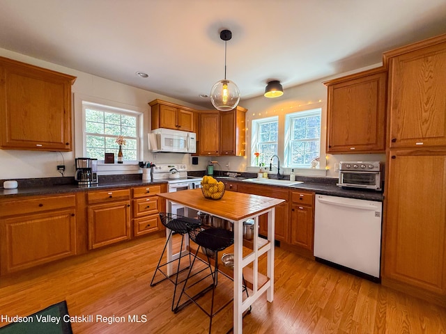 kitchen with brown cabinets, white appliances, light wood-type flooring, and a sink