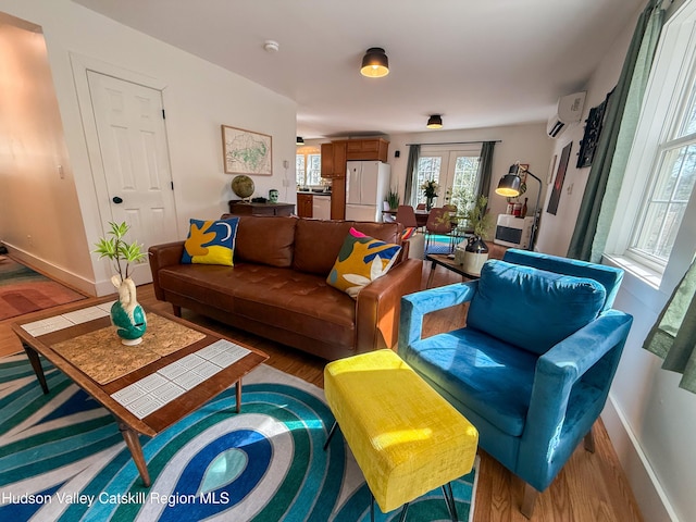 living room featuring wood finished floors, french doors, baseboards, and a wall mounted air conditioner