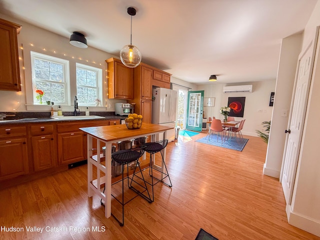 kitchen with a sink, dark countertops, freestanding refrigerator, light wood finished floors, and a healthy amount of sunlight