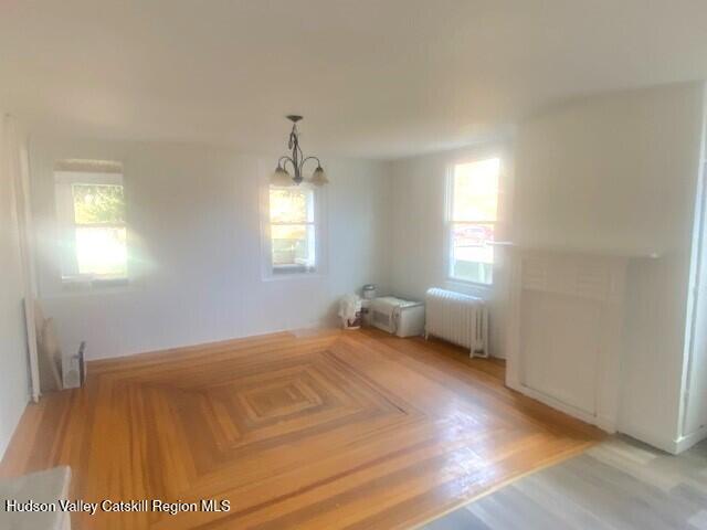 unfurnished dining area featuring a chandelier, radiator heating unit, a healthy amount of sunlight, and hardwood / wood-style floors