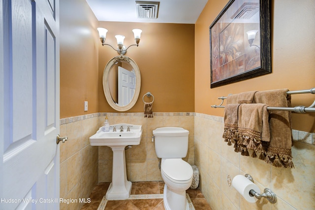 half bath with tile patterned flooring, visible vents, tile walls, and toilet