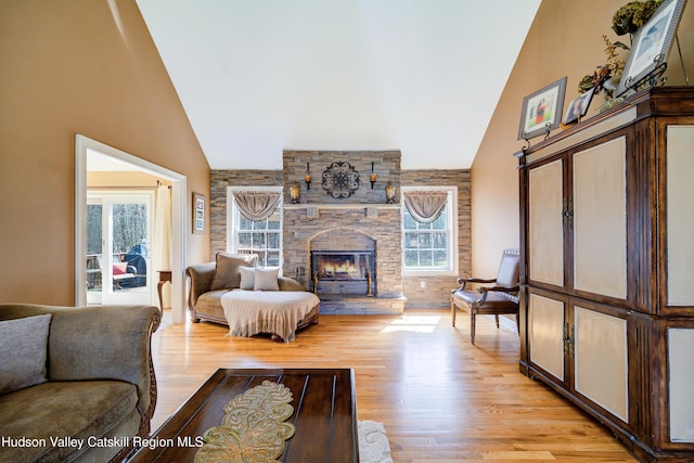 living room featuring a wealth of natural light, high vaulted ceiling, light wood-style flooring, and a stone fireplace