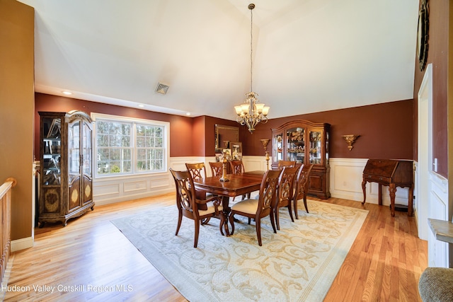 dining area featuring light wood-type flooring, vaulted ceiling, an inviting chandelier, a wainscoted wall, and visible vents