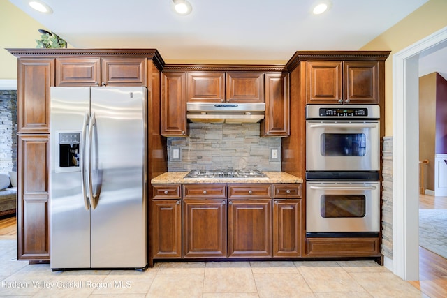 kitchen with tasteful backsplash, appliances with stainless steel finishes, under cabinet range hood, recessed lighting, and light stone countertops