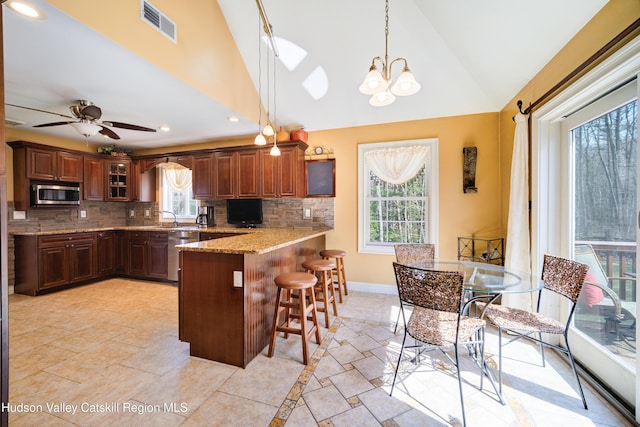 kitchen featuring a kitchen breakfast bar, a peninsula, glass insert cabinets, visible vents, and appliances with stainless steel finishes