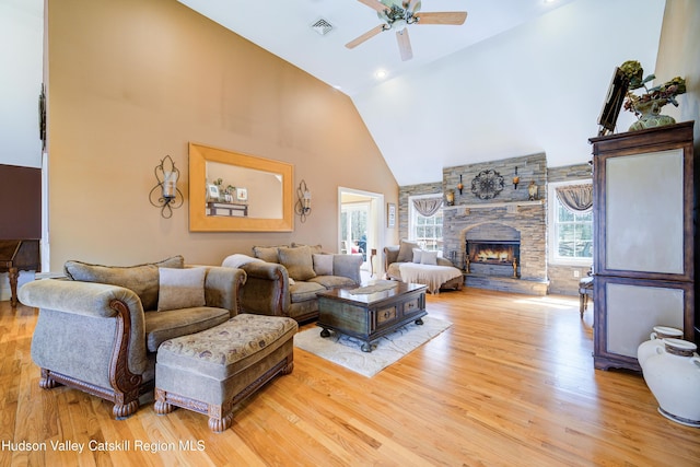 living room with light wood-type flooring, a fireplace, a ceiling fan, visible vents, and high vaulted ceiling