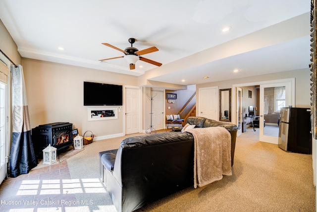 living area with a wood stove, a ceiling fan, recessed lighting, light carpet, and stairs