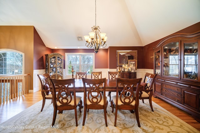 dining space featuring visible vents, an inviting chandelier, light wood-type flooring, a wainscoted wall, and lofted ceiling