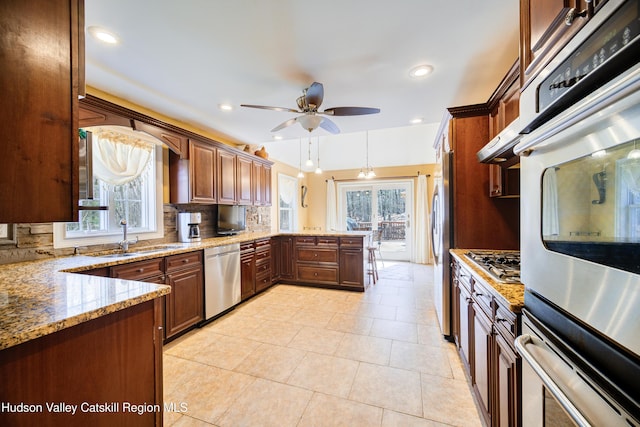 kitchen with a ceiling fan, a peninsula, stainless steel appliances, backsplash, and light stone counters
