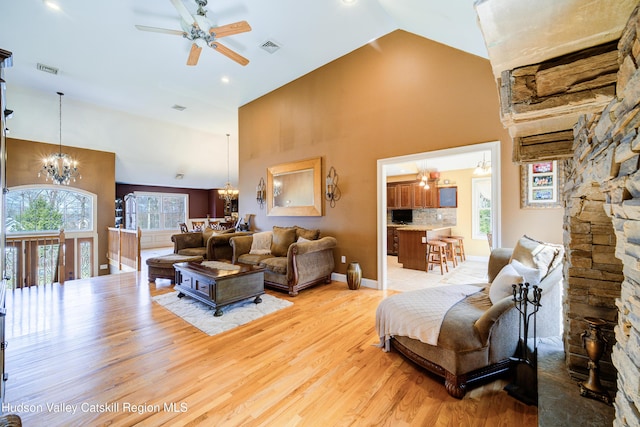 living room featuring high vaulted ceiling, light wood finished floors, ceiling fan with notable chandelier, and a healthy amount of sunlight
