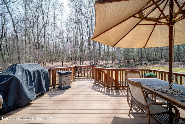wooden terrace featuring a forest view, outdoor dining space, and a grill