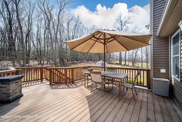 wooden deck featuring outdoor dining area, an outbuilding, and a storage unit