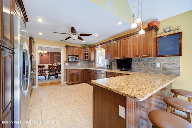 kitchen with a peninsula, backsplash, brown cabinets, a kitchen bar, and appliances with stainless steel finishes