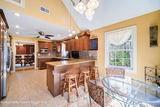 kitchen featuring visible vents, appliances with stainless steel finishes, a peninsula, brown cabinets, and light stone countertops