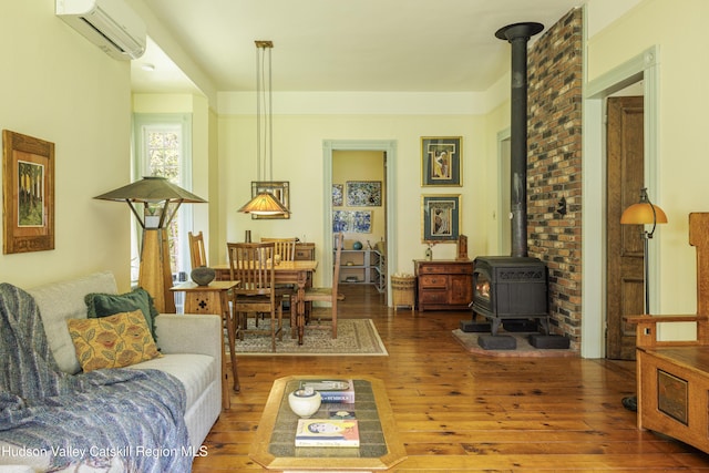 living room with a wall unit AC, a wood stove, and wood-type flooring