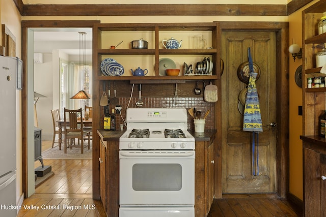 kitchen with white gas range oven, freestanding refrigerator, dark wood finished floors, dark countertops, and open shelves