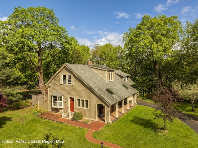 view of front of home with a front yard, a chimney, a shingled roof, and view of wooded area