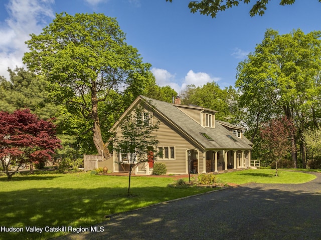 view of front facade featuring a porch, a front yard, a chimney, and view of scattered trees