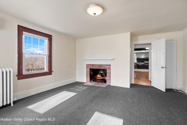 unfurnished living room featuring radiator, dark carpet, and a brick fireplace