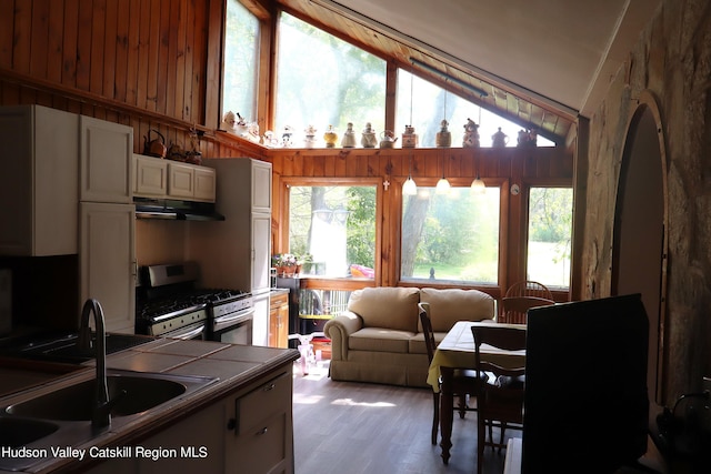 kitchen with under cabinet range hood, a sink, open floor plan, tile counters, and gas stove