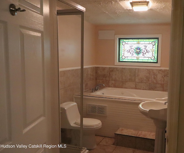 full bath featuring a garden tub, tile walls, toilet, a textured ceiling, and tile patterned flooring