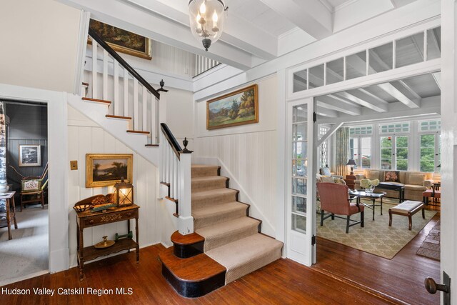 staircase featuring hardwood / wood-style floors, wood walls, and beamed ceiling