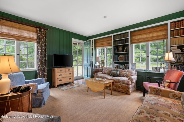 living room with light carpet, built in features, a healthy amount of sunlight, and wood walls