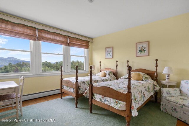 bedroom with hardwood / wood-style floors, a mountain view, baseboard heating, and multiple windows