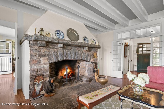 living room with beamed ceiling, a stone fireplace, wood-type flooring, and crown molding