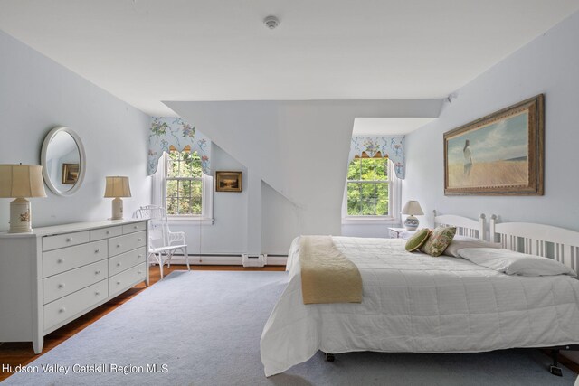 bedroom with multiple windows, wood-type flooring, and a baseboard heating unit