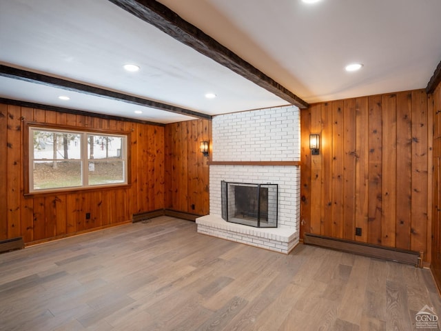 unfurnished living room featuring baseboard heating, beamed ceiling, wood finished floors, a fireplace, and wooden walls