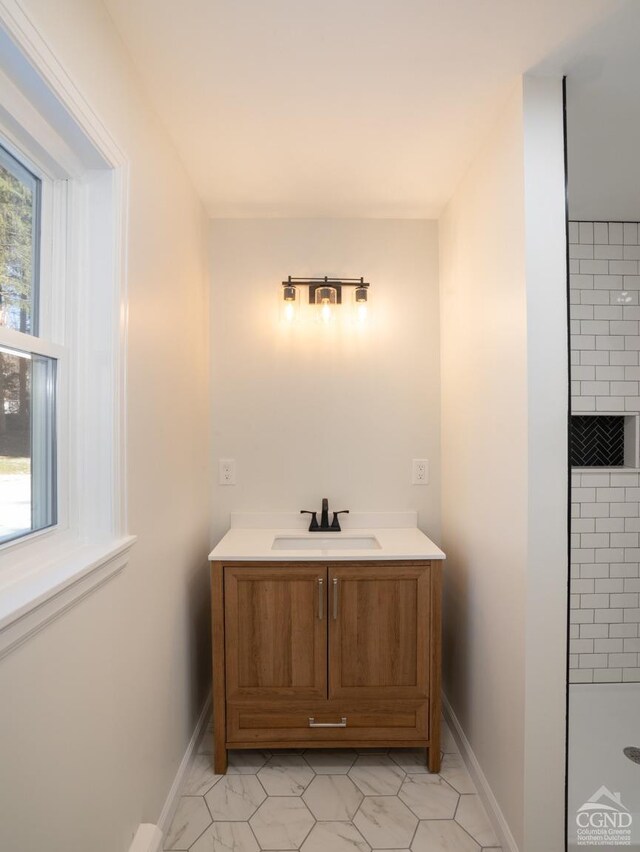 full bath with baseboards, vanity, and tiled shower