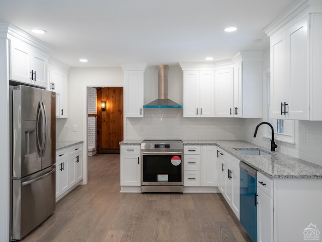kitchen with stainless steel appliances, wall chimney range hood, a sink, light wood-style floors, and backsplash