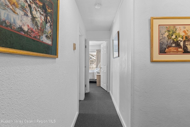 hall featuring dark carpet, baseboards, and a textured wall