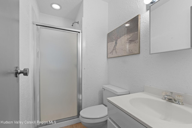 bathroom with a textured wall, vanity, toilet, and a stall shower