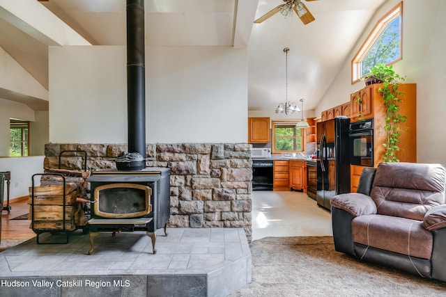 living room with ceiling fan with notable chandelier, high vaulted ceiling, and a wood stove