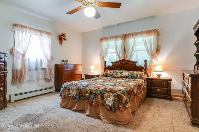 bedroom with ceiling fan, baseboard heating, light carpet, and multiple windows