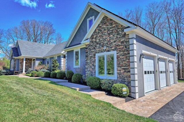 52 Hadley Dr, New Baltimore, NY 12087 - view of side of home featuring stone siding, stucco siding, a lawn, driveway, and an attached garage