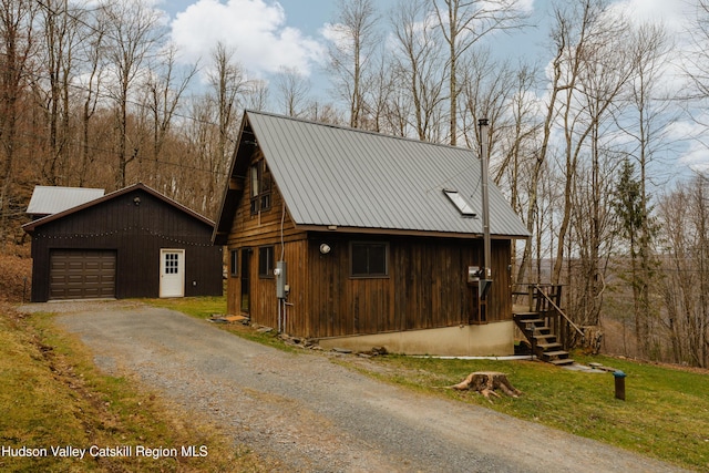 view of side of home with aphalt driveway, a garage, a lawn, an outdoor structure, and metal roof