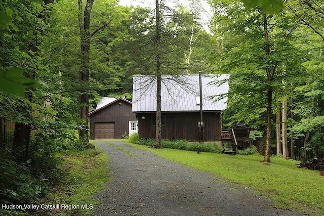 view of side of home featuring an attached garage, aphalt driveway, a wooden deck, a lawn, and a wooded view