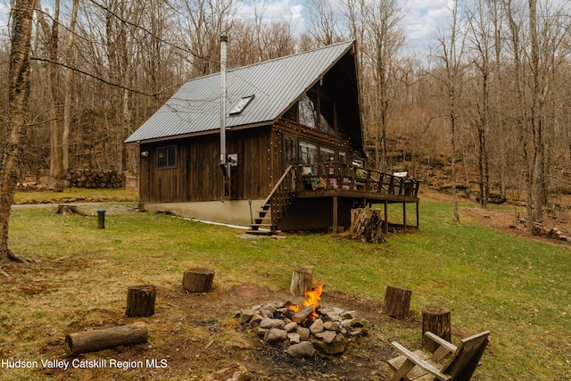 view of side of home featuring metal roof, a wooden deck, a yard, a fire pit, and stairs